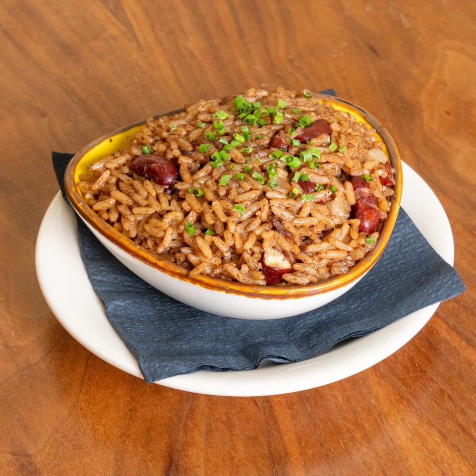 Seasoned rice with sliced sausage and green onions served in a ceramic dish on a slate-lined plate.