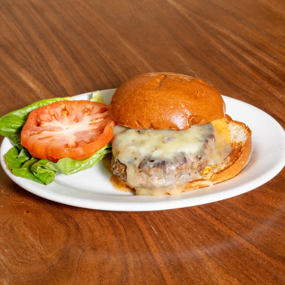 Cheeseburger with melted cheese, lettuce, and tomato served on a white plate atop a wooden table.